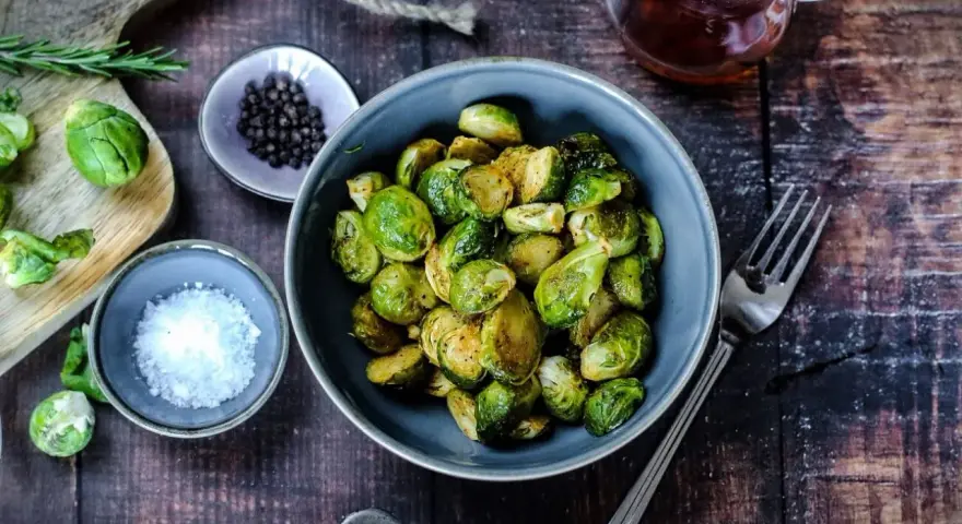 Gerösteter Rosenkohl in einer Schüssel, bereit für leckere Rezepte mit Rosenkohl. Daneben Salz, Pfeffer und ein Glas Sirup.