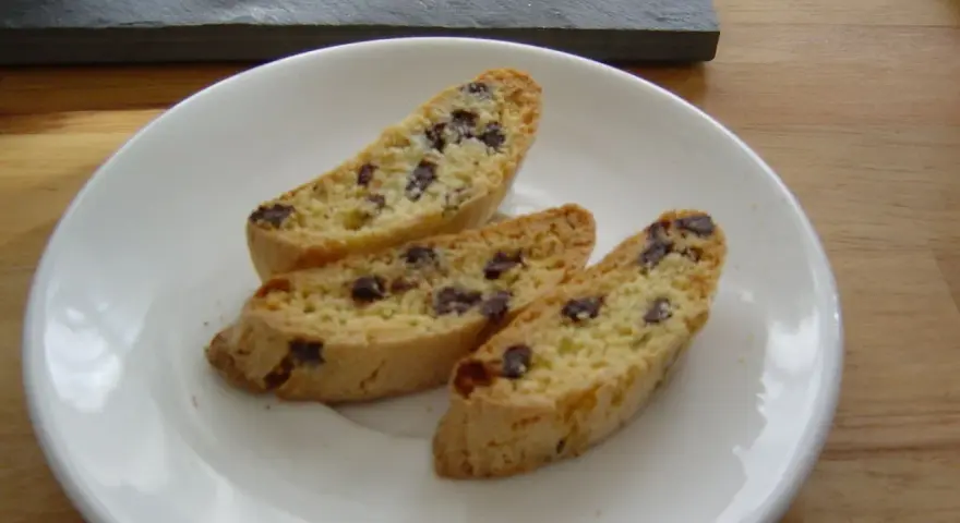 Drei knusprige Cantuccini mit Schokolade liegen auf einem weißen Teller.