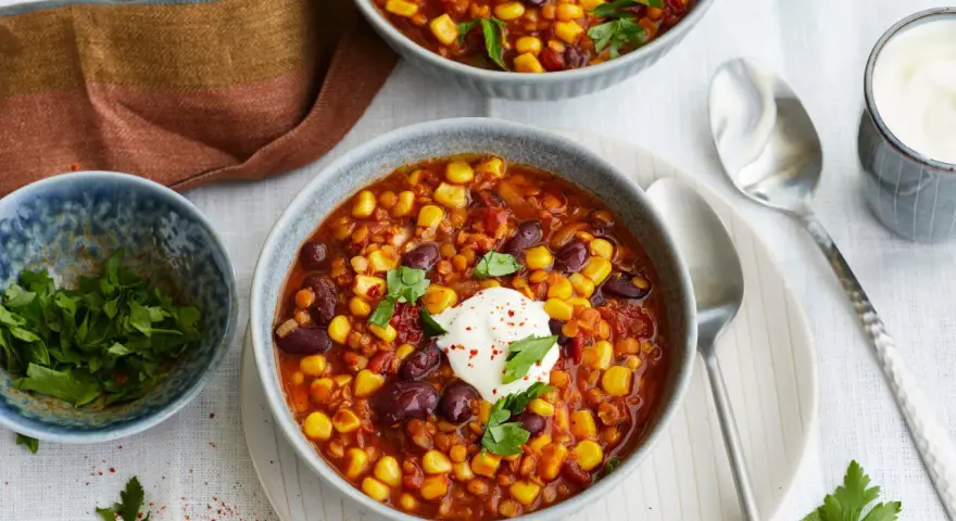 Herzhaftes Chili sin Carne mit Mais, Bohnen und Linsen, garniert mit einem Klecks Sauerrahm und frischer Petersilie.