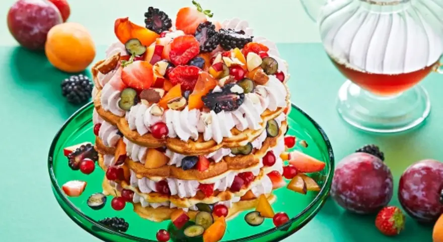 Eine mehrstöckige Waffeltorte mit Mascarpone-Creme, Beeren, Pfirsichen und Nüssen, garniert mit frischen Früchten.