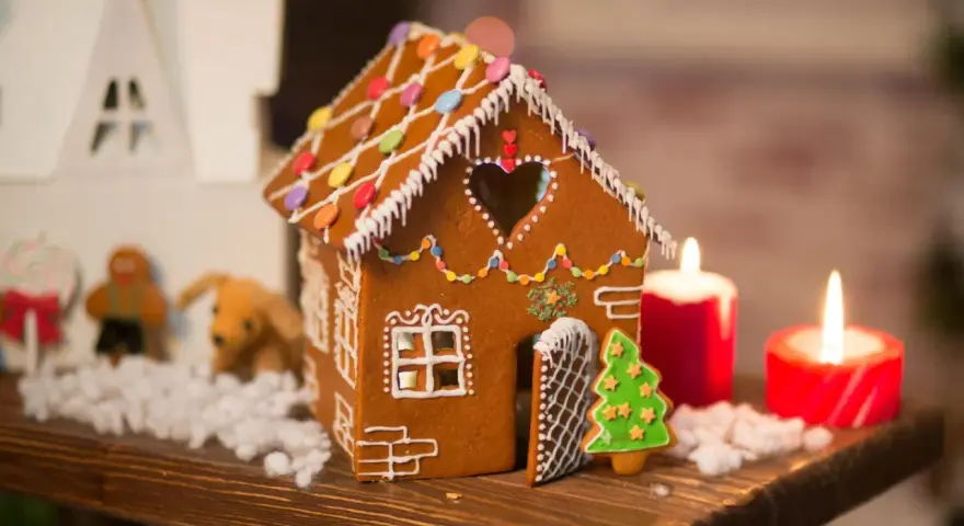 Ein zauberhaftes Lebkuchenhaus, das Lust macht, es selber zu machen. Verziert mit bunten Smarties und Zuckerguss, steht es neben Kerzen und Weihnachtsfiguren.