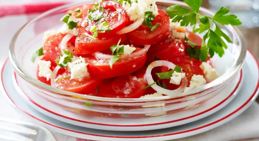 Frischer Tomaten Feta Salat mit Zwiebelringen und Petersilie, garniert mit schwarzem Pfeffer und Meersalz.