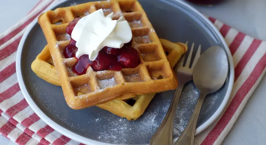 Zwei Hefewaffeln mit Trockenhefe, garniert mit Kirschkompott und Sahne, bestäubt mit Puderzucker.