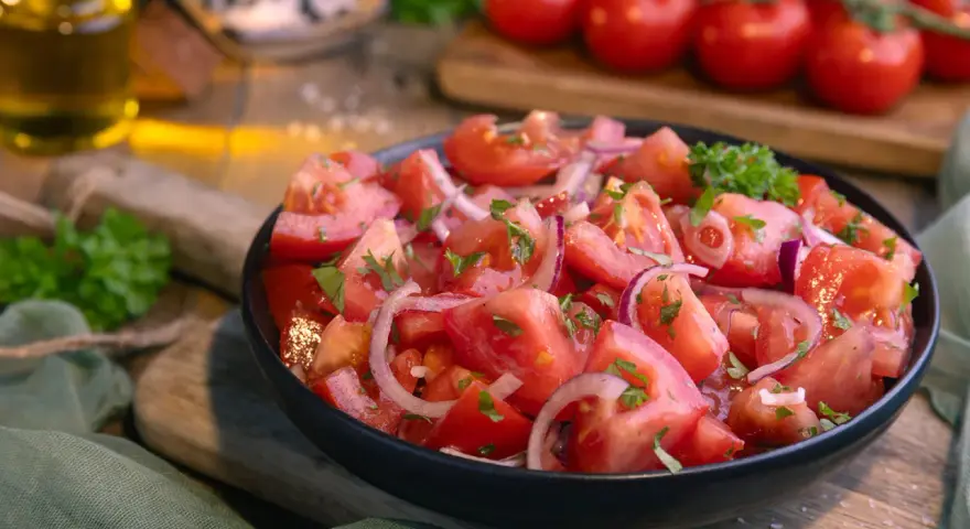 Frischer Tomatensalat mit roten Zwiebeln und Petersilie, serviert in einer schwarzen Schüssel. Das Tomatensalat Dressing ist leicht und würzig.