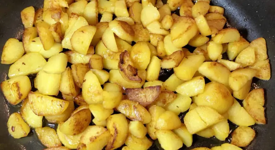 Goldbraune bratkartoffeln aus gekochten kartoffeln brutzeln in der Pfanne. Sie sind knusprig und duften herrlich.