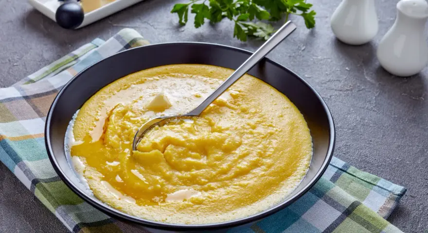 Cremige Polenta mit Butter, ein einfaches und köstliches polenta rezept, serviert in einer schwarzen Schüssel auf kariertem Tuch.