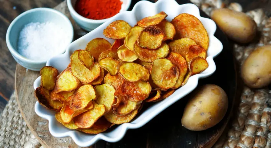 Selbstgemachte Kartoffelchips, goldbraun und knusprig, mit Salz und Paprikapulver daneben. So einfach kannst du Chips selber machen!