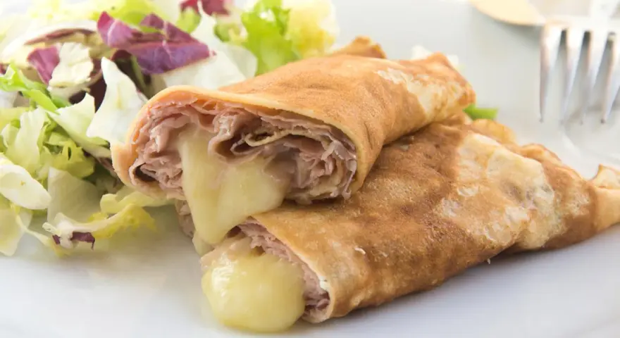 Zwei herzhafte Pfannkuchen mit Schinken und geschmolzenem Käse, serviert mit einem frischen Salat.