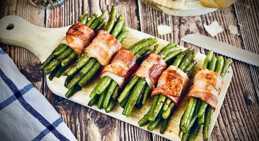 Grüne Bohnen, umwickelt mit knusprigem Speck, ein köstliches Speckbohnen Rezept, serviert auf einem Holzbrett.