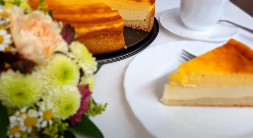 Ein köstliches Eierschecke-Rezept: Ein goldbrauner Kuchen mit cremiger Füllung, daneben eine Tasse Kaffee und ein Blumenstrauß.