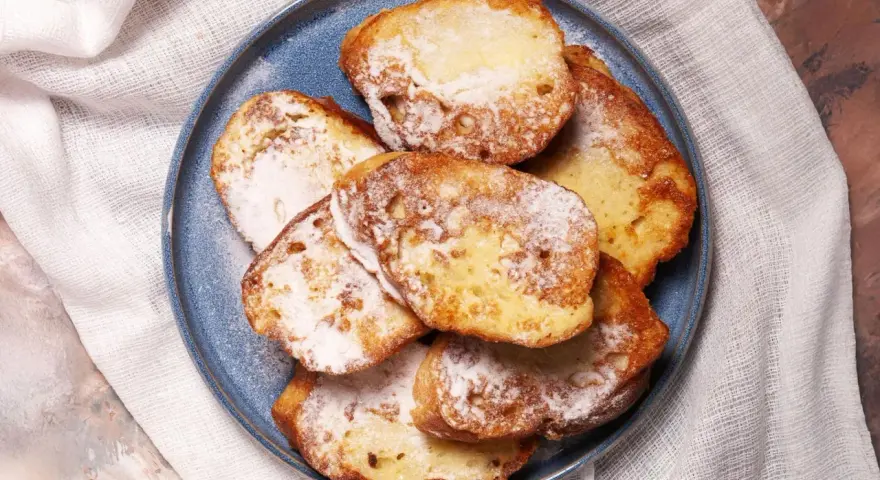 Armer Ritter, goldbraun gebacken und mit Puderzucker bestäubt, liegen auf einem blauen Teller.