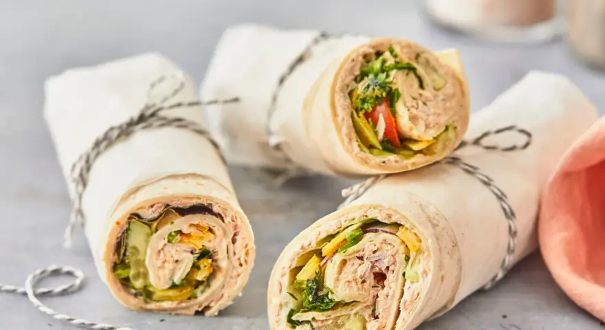 Drei leckere Thunfisch-Wraps, gefüllt mit Salat, Gurke und Tomate, sind in Papier gewickelt und mit Schnur verschnürt.