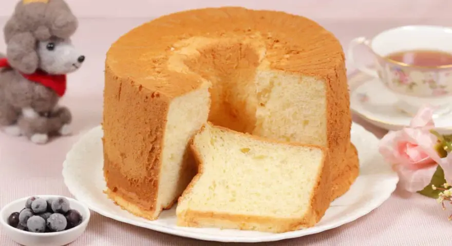 Ein luftiger Chiffon-Kuchen mit einer Scheibe daneben, serviert mit Beeren und Tee.