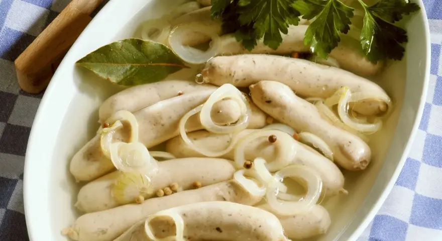 Saure Zipfel in einer Schüssel mit Zwiebelringen, Lorbeerblatt und Petersilie.