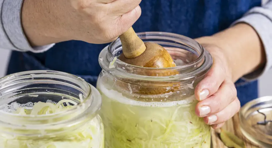Hände pressen Kohl für ein einfaches Sauerkraut Rezept in ein Glas.