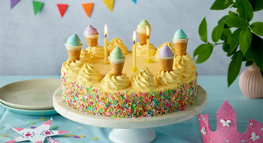 Bunte Torte mit Streuseln und Eiswaffel-Deko, perfekt für kinder torten rezepte einfach. Kerzen brennen, eine märchenhafte Feier beginnt.