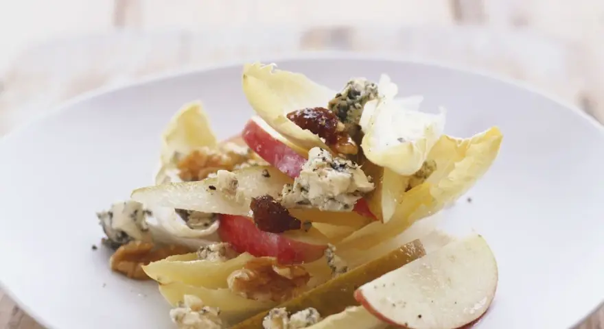 Ein köstlicher chicoree salat mit Äpfeln, Birnen, Blauschimmelkäse und Walnüssen auf einem weißen Teller.