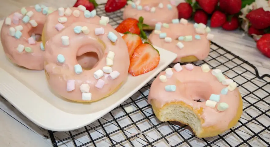 Leckere Donuts mit rosa Glasur und Marshmallows, perfekt für ein schnelles Donuts Rezept aus dem Backofen. Frische Erdbeeren garnieren das süße Gebäck.