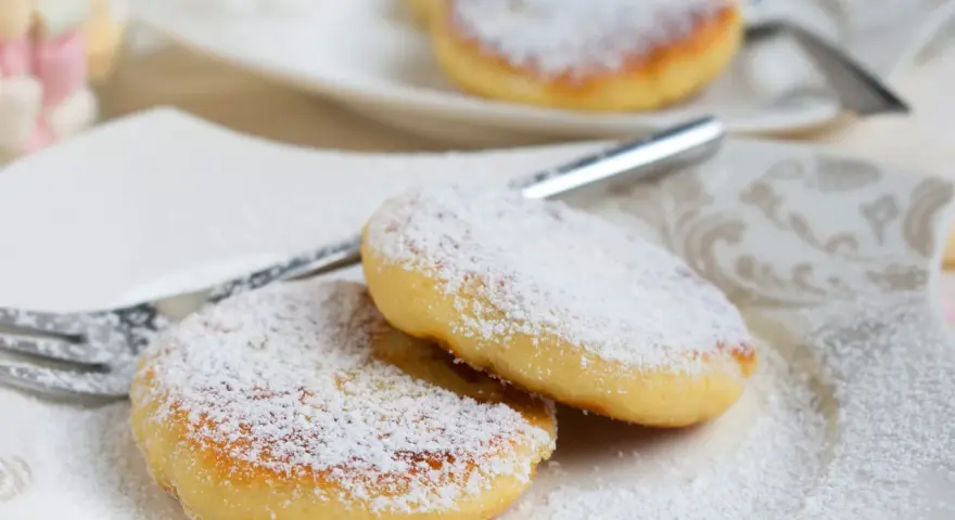 Zwei goldbraune Quarkkeulchen, bestäubt mit Puderzucker, liegen auf einem Teller. Ein einfaches Quarkkeulchen Rezept für süße Momente.