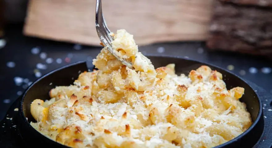 Ein Gabel hebt cremiges, überbackenes Mac n Cheese aus einer Pfanne. Dieses amerikanische Original-Rezept ist ein Genuss!