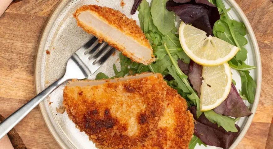 Knuspriges Kohlrabi-Schnitzel mit Salat und Zitrone auf einem Teller.