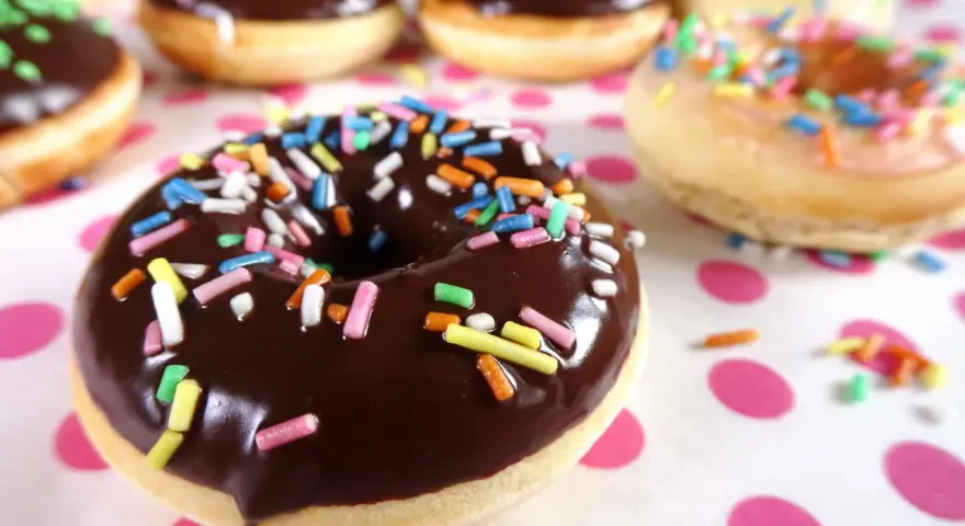 Bunte Streusel auf Schokoladen- und Zuckerguss-Donuts, die an ein leckeres Donut Teig Rezept erinnern.
