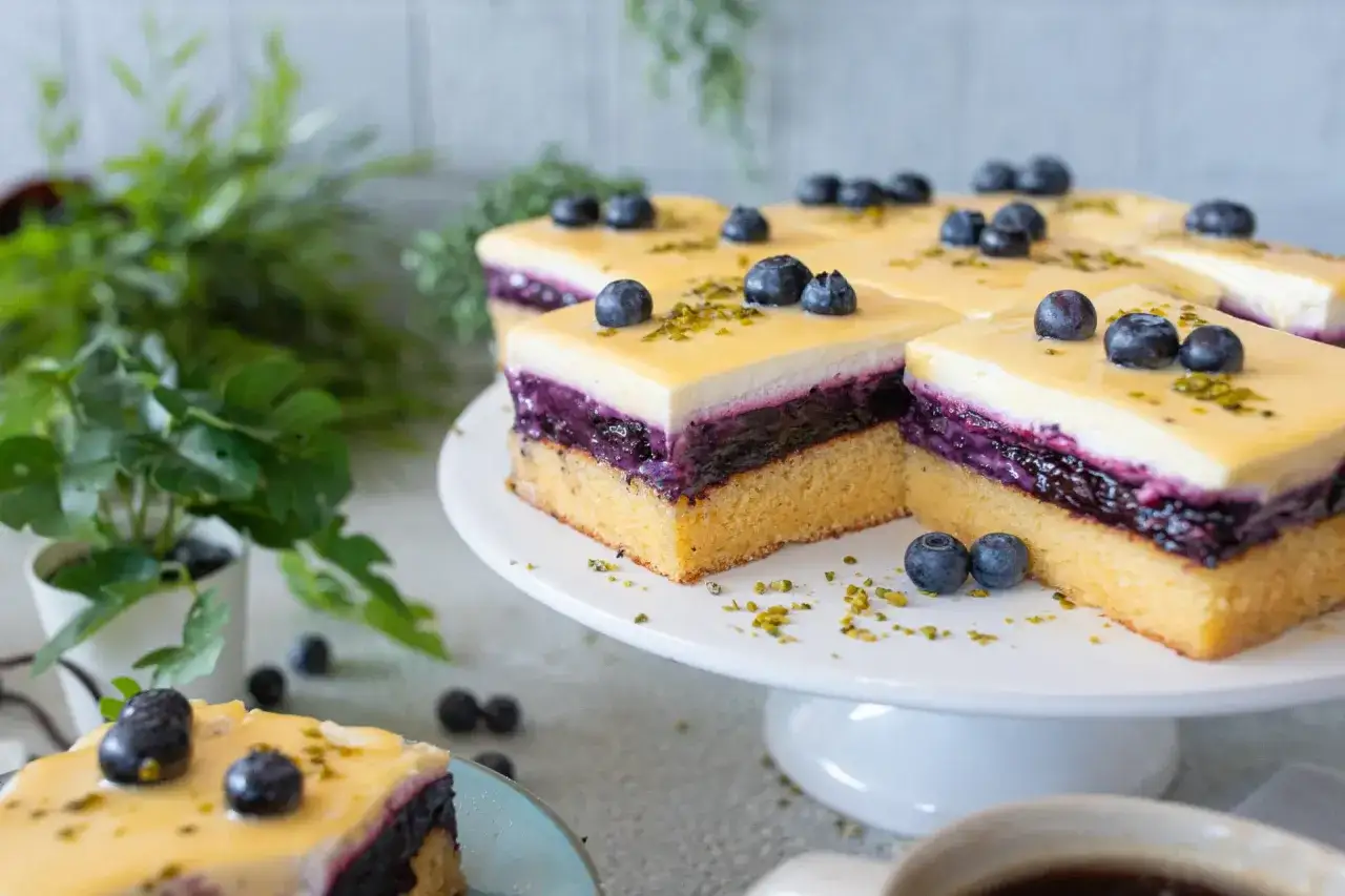 Saftiger Heidelbeerkuchen Landfrauenart mit Blaubeeren und gelber Glasur, garniert mit Pistazien.