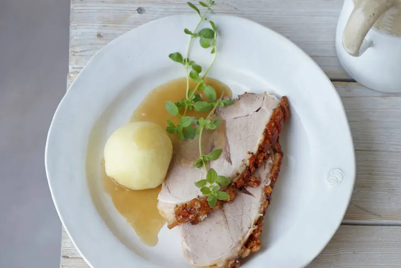Ein Teller mit saftigem Schweinebraten, einer Kartoffelkn&ouml;del und So&szlig;e. Ein perfektes Schweinebraten Rezept f&uuml;r jeden Anlass.