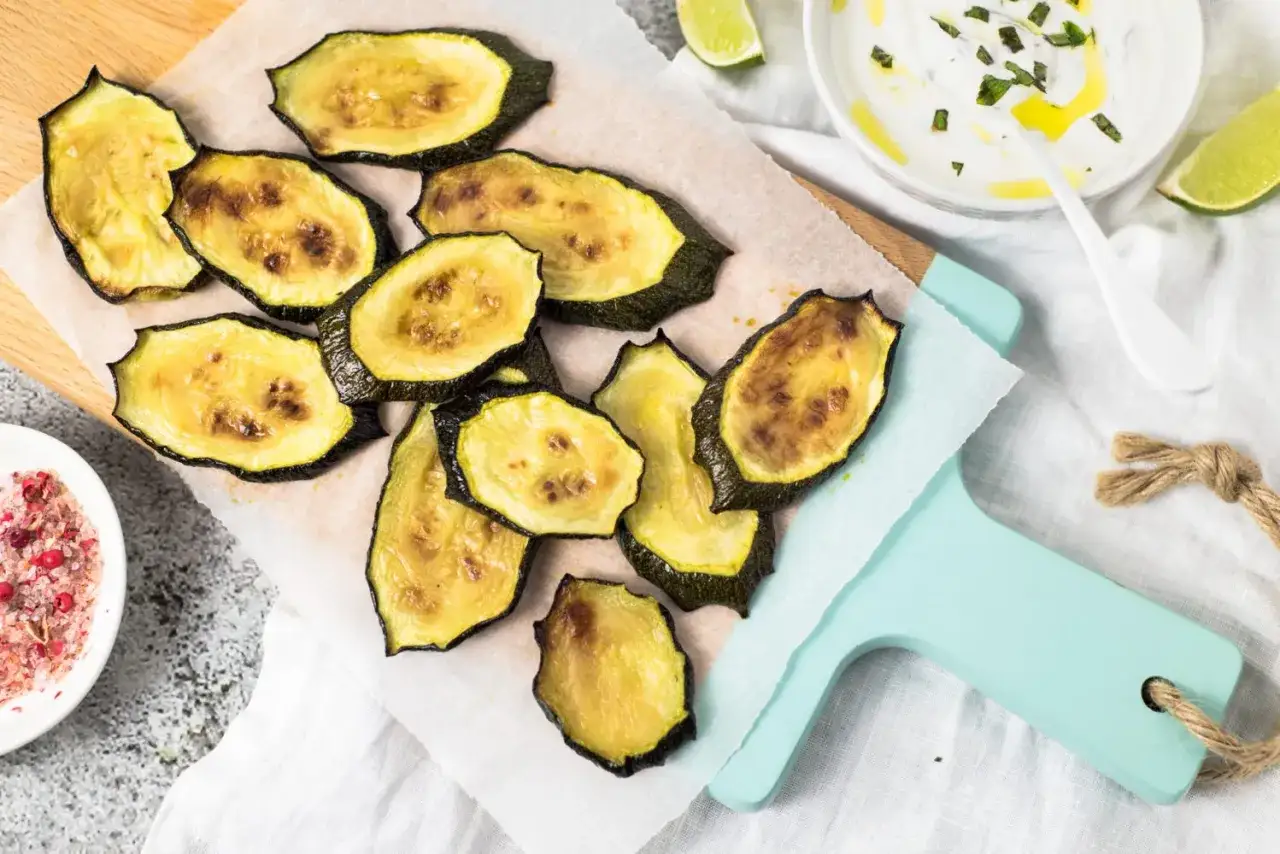 Ger&ouml;stete Zucchinischeiben auf Backpapier, perfekt f&uuml;r schnelle zucchini rezepte aus dem backofen. Dazu ein Dip und rosa Pfeffer.