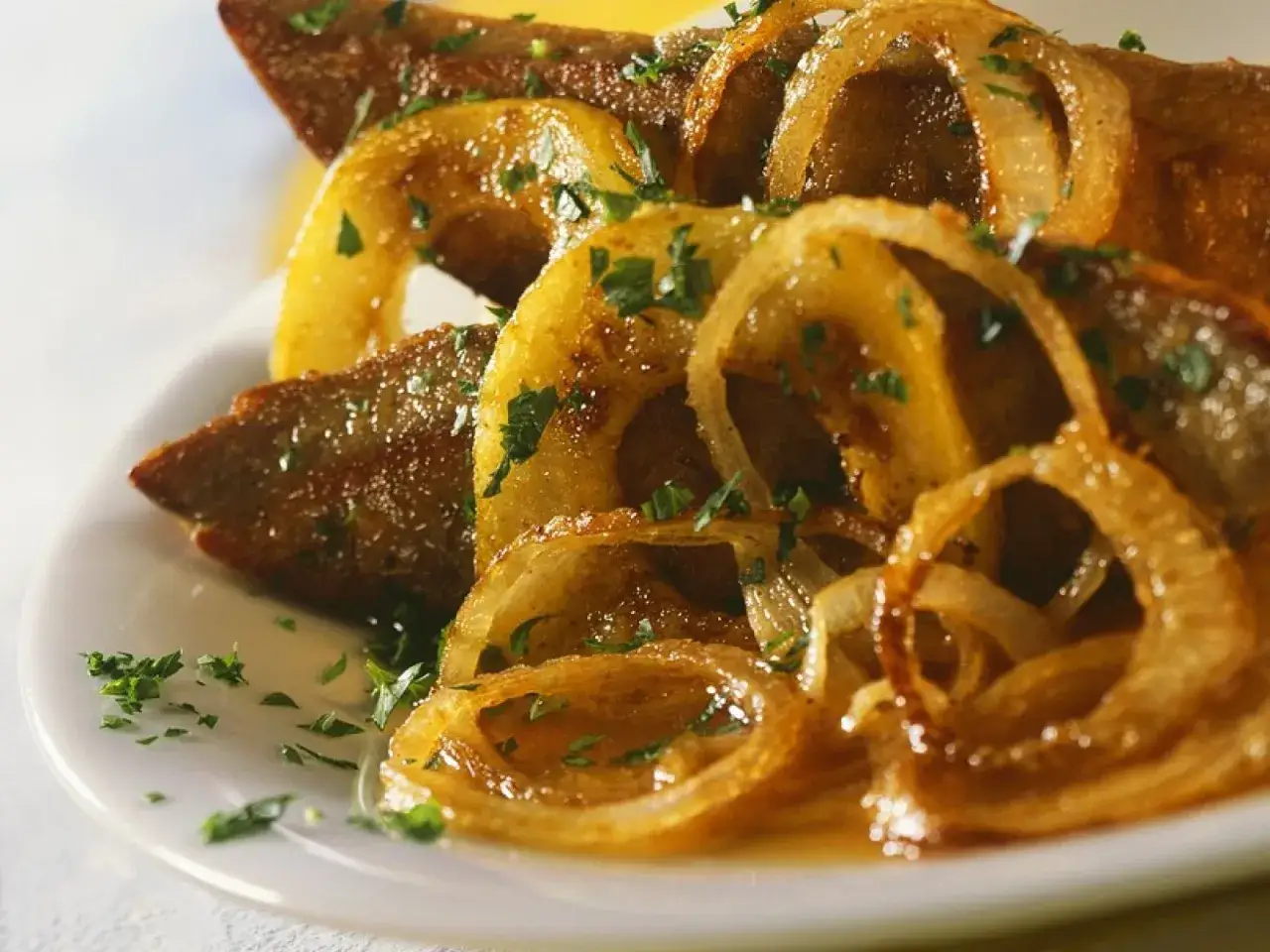 Leber braten mit karamellisierten Zwiebelringen und Petersilie auf einem wei&szlig;en Teller. Ein Klassiker, der Appetit macht.