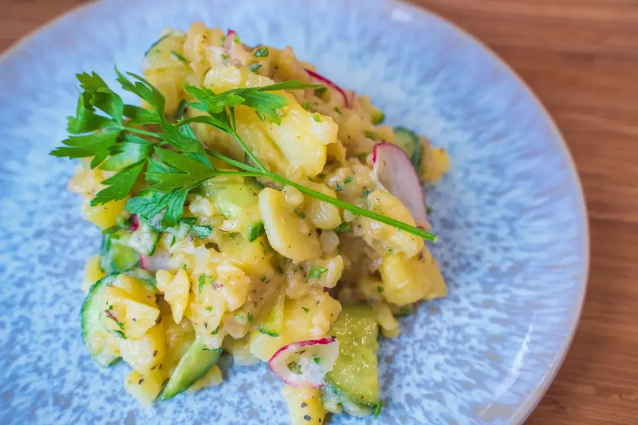 Ein köstlicher Kartoffelsalat mit Gurken, garniert mit frischer Petersilie, auf einem blauen Teller.