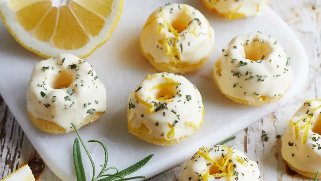 Mini Gugelhupf-Rezept: Kleine, mit wei&szlig;er Glasur und Zitronenzesten verzierte K&uuml;chlein, daneben eine Zitronenh&auml;lfte und Rosmarin.