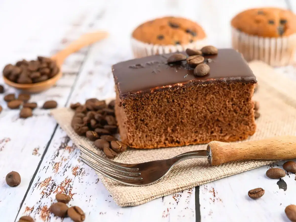 Ein Stück Schokoladenkuchen mit Kaffee-Aroma, garniert mit Kaffeebohnen. Daneben eine Löffel voller Bohnen und zwei Muffins. Ein köstlicher Bierkuchen-Moment.