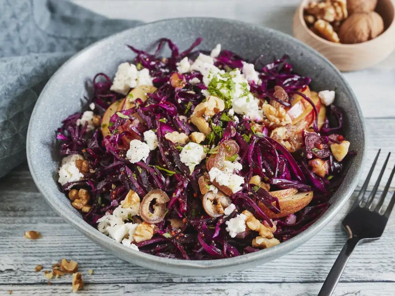Ein bunter rotkohl salat mit &Auml;pfeln, N&uuml;ssen und Feta in einer grauen Sch&uuml;ssel.