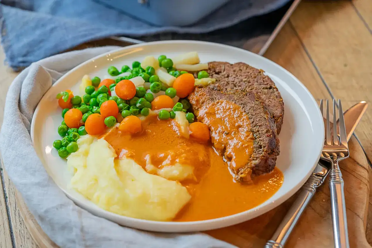 Ein saftiger Hackbraten mit Kartoffelpüree, Erbsen und Karotten in einer cremigen Sauce. Ein klassisches Hackbraten Rezept für ein herzhaftes Essen.