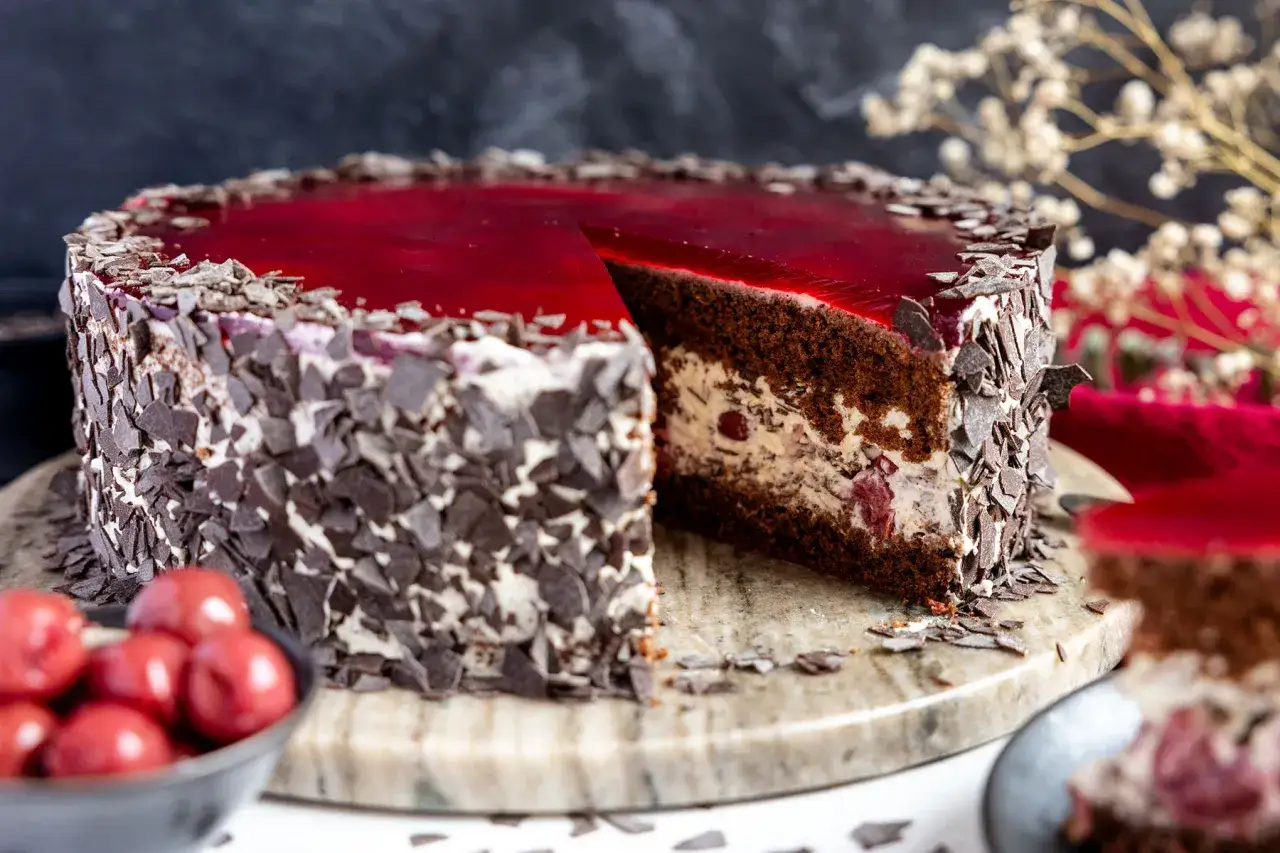 Eine k&ouml;stliche Schoko Stracciatella Torte mit Kirschen und rotem Tortenguss, dekoriert mit Schokost&uuml;ckchen.
