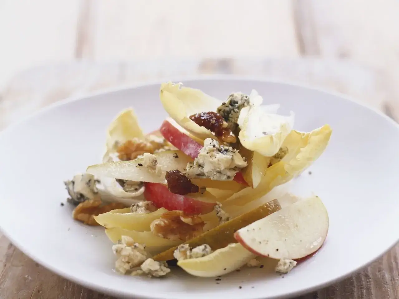 Ein k&ouml;stlicher chicoree salat mit &Auml;pfeln, Birnen, Waln&uuml;ssen und Blauschimmelk&auml;se auf einem wei&szlig;en Teller.