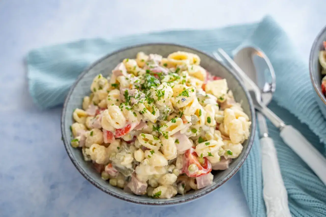 Sch&uuml;ssel mit Nudelsalat, garniert mit Petersilie. Das cremige nudelsalat dressing verbindet Nudeln, Schinken, Erbsen und Tomaten zu einem leckeren Gericht.