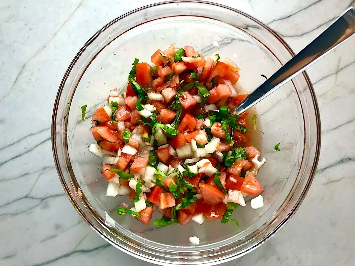 Frischer Tomatensalat mit Zwiebeln und Basilikum, perfekt f&uuml;r jedes Tomatensalat Rezept. Ein L&ouml;ffel liegt darin.