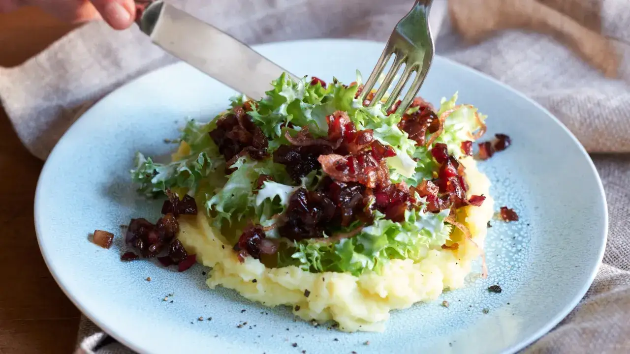 Kartoffelbrei mit Salat und karamellisierten Zwiebeln, inspiriert von Blutampfer-Rezepten. Ein Messer und eine Gabel sind bereit zum Essen.