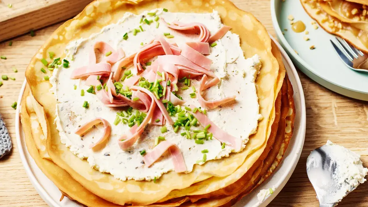 Stapel herzhafter Pfannkuchen mit cremiger F&uuml;llung, Schinkenstreifen und Schnittlauch.