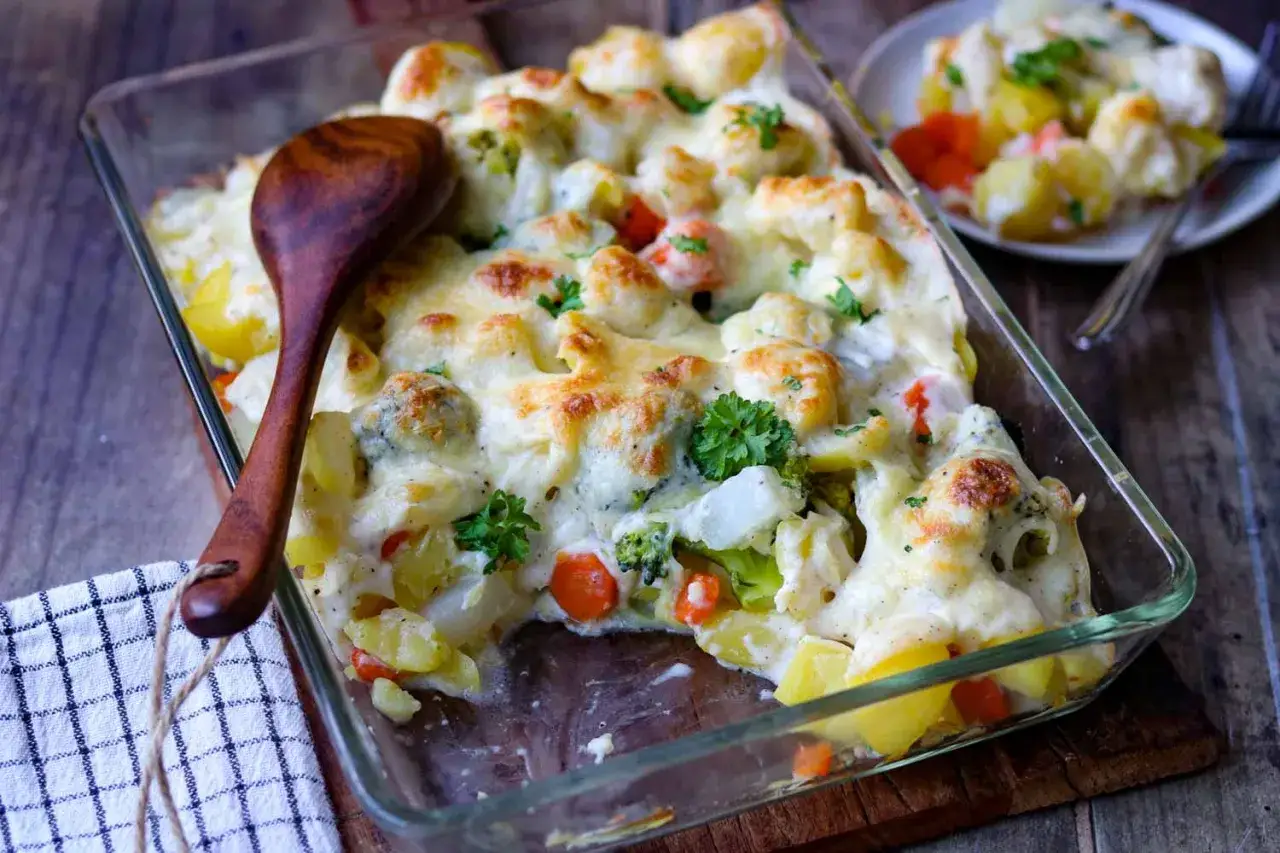 Herzhafter vegetarischer Auflauf mit Kartoffeln, Brokkoli, Blumenkohl und Karotten, überbacken mit Käse. Ein Holzlöffel liegt bereit.