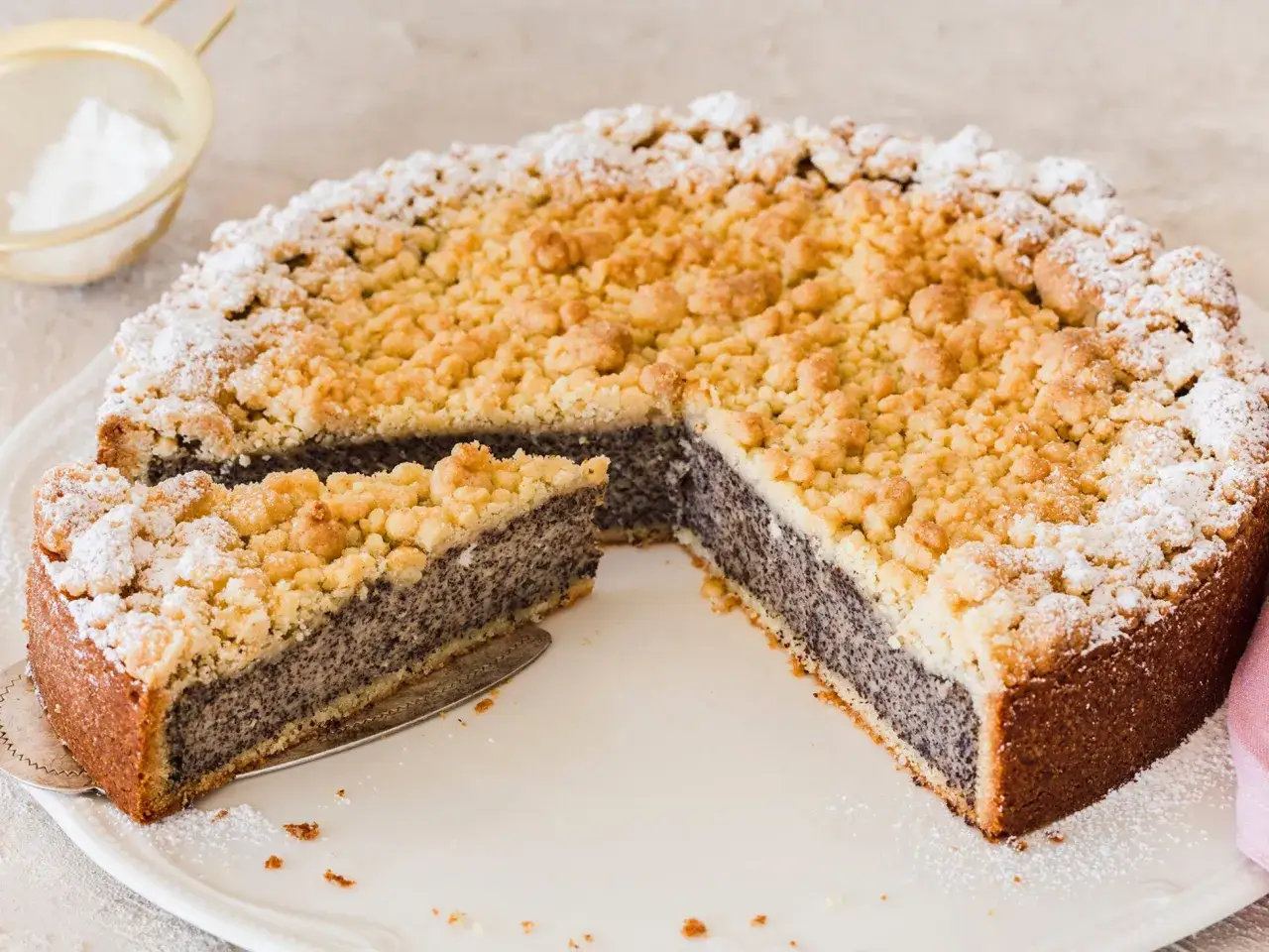 Ein saftiger Kuchen mit Mohnback, bestreut mit Puderzucker. Ein Stück wurde bereits herausgeschnitten.