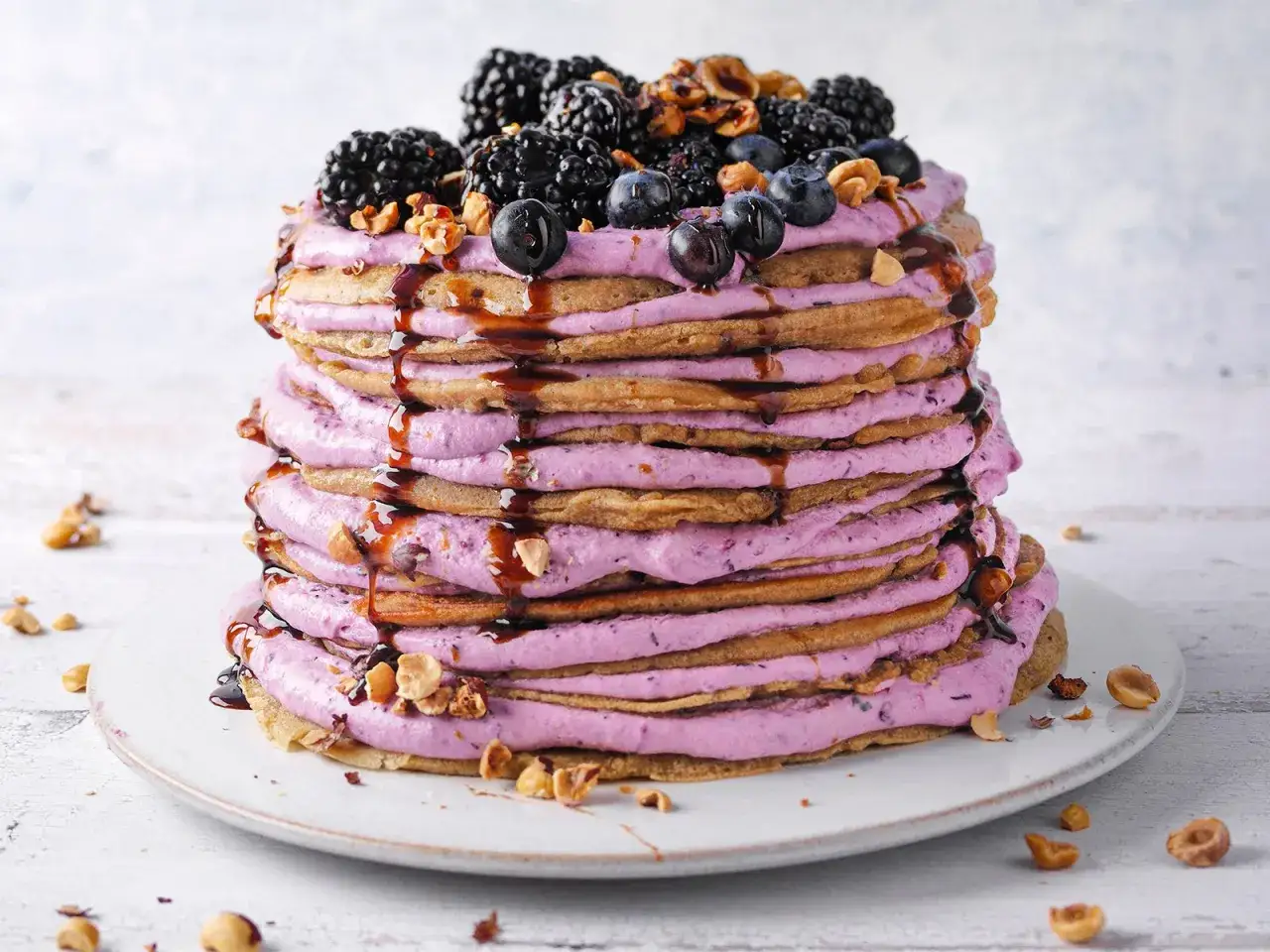 Hohe Pfannkuchen-Torte mit lila Beerencreme, Brombeeren, Blaubeeren und N&uuml;ssen, betr&auml;ufelt mit Schokoladensirup.