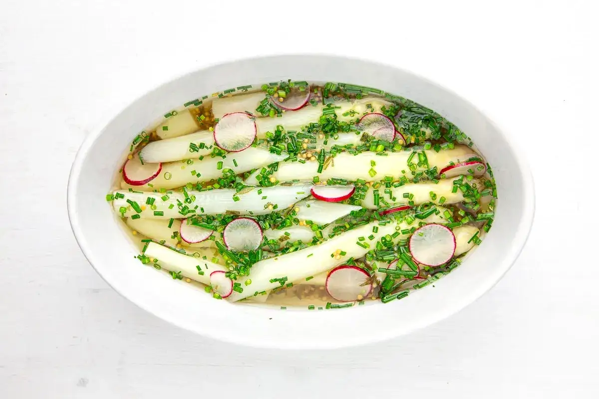 Klassisches Spargelsalat Rezept: Weiße Spargelstangen mariniert mit Radieschenscheiben und Schnittlauch in einer leichten Vinaigrette.