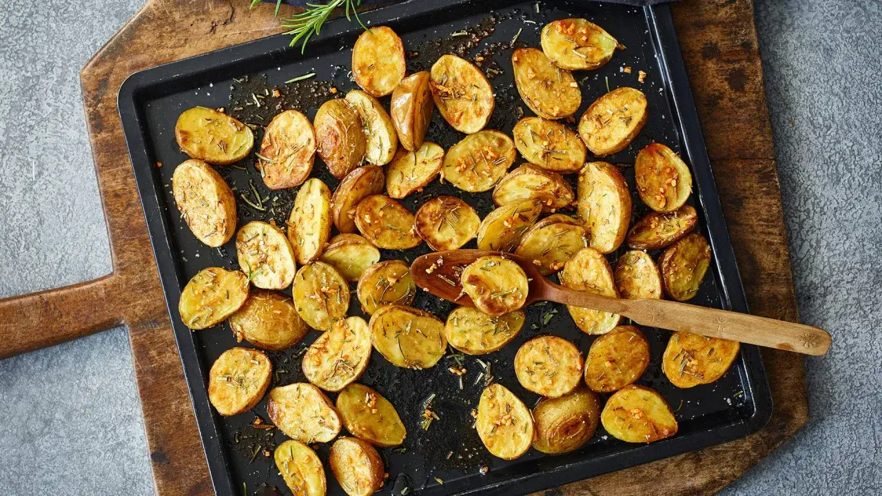 Goldbraune, knusprige Rosmarinkartoffeln mit Knoblauch und Kr&auml;utern auf einem Backblech, bereit zum Servieren.