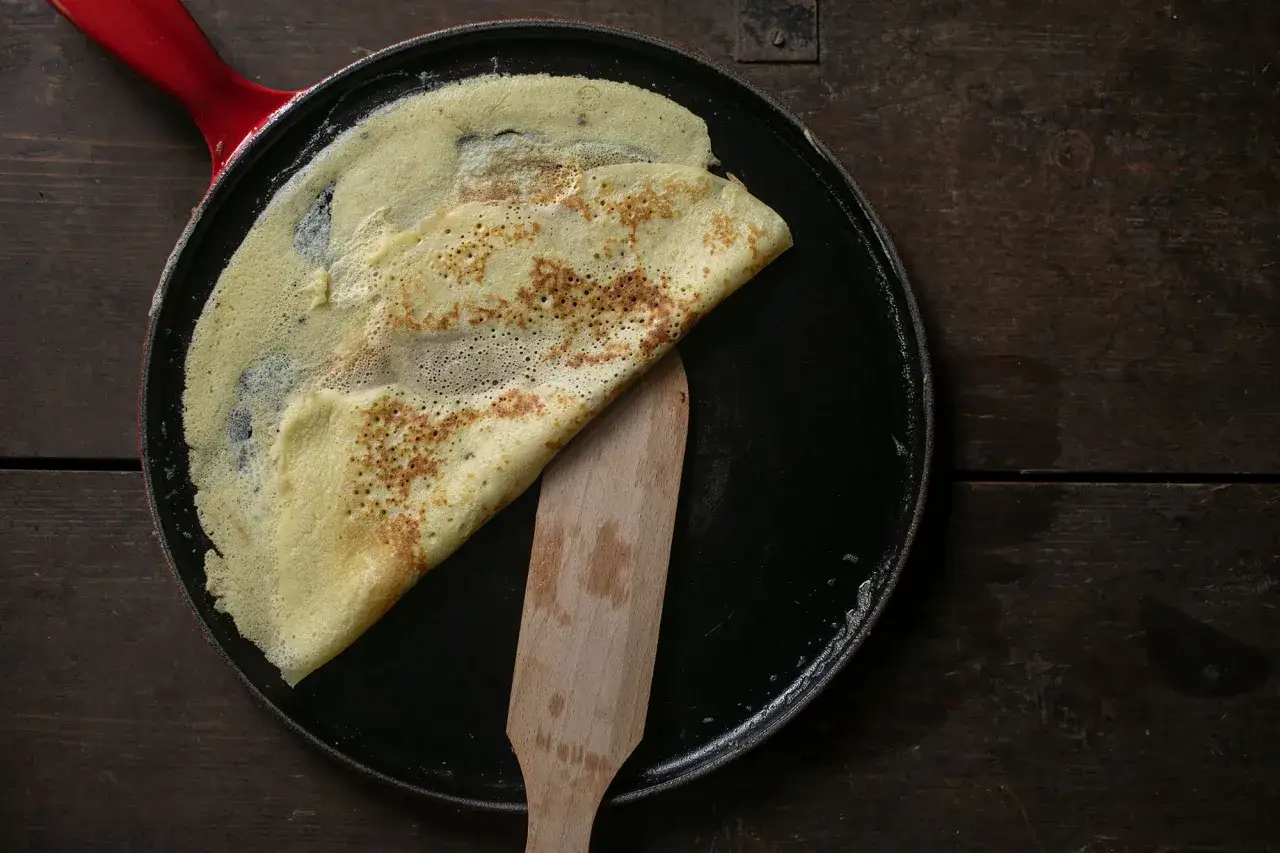 Ein goldbrauner Cr&ecirc;pe wird in einer Pfanne mit rotem Griff gefaltet. Das einfache Cr&ecirc;pes Rezept gelingt so perfekt.