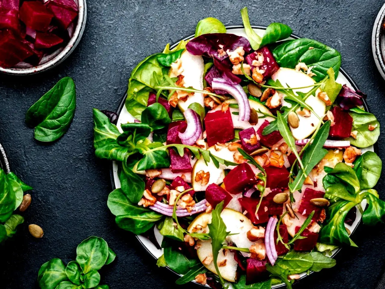 Bunter rote Bete Salat mit Birnenspalten, Waln&uuml;ssen und roten Zwiebeln auf einem Bett aus frischem Gr&uuml;n.