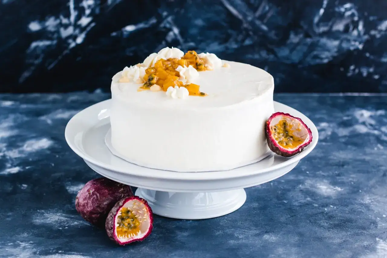 Eine wei&szlig;e Maracuja Torte mit frischer Maracuja-Frucht und Sahnetupfern, umgeben von ganzen und halbierten Maracujas.