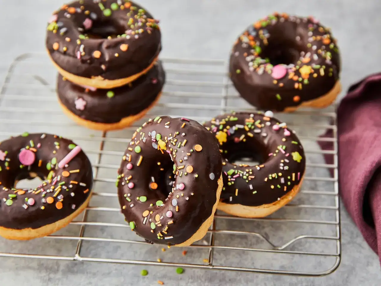 Schokoladen-Donuts mit bunten Streuseln auf einem Kuchengitter. Ein köstliches Rezept für selbstgemachte Donuts aus dem Backofen.